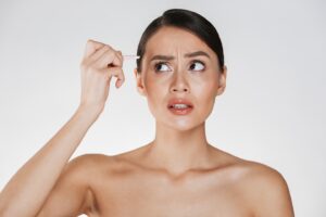 Woman applying skincare serum with a dropper to her temple, looking puzzled.